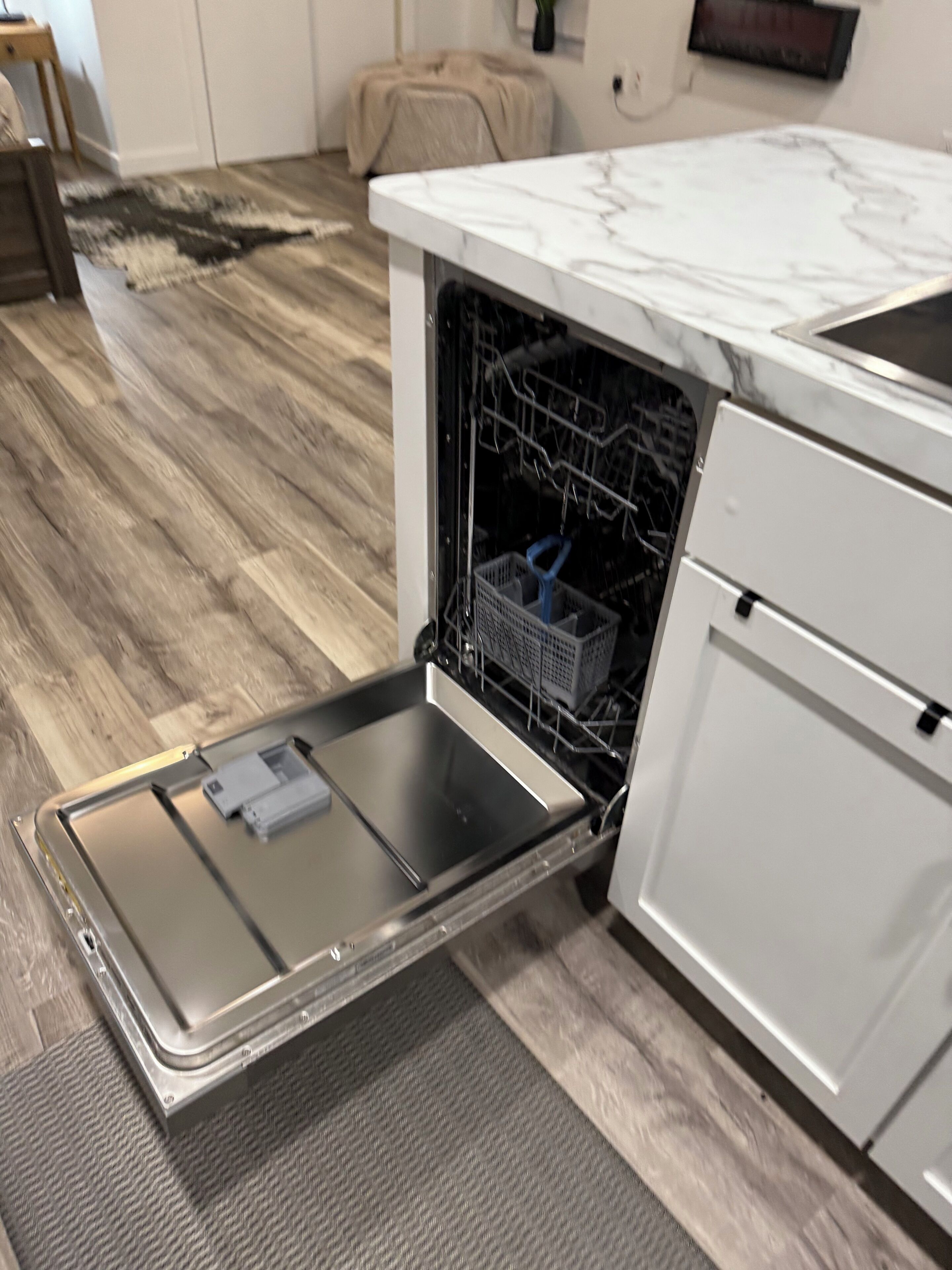 A kitchen with a dishwasher, a marble countertop, and a patterned rug.