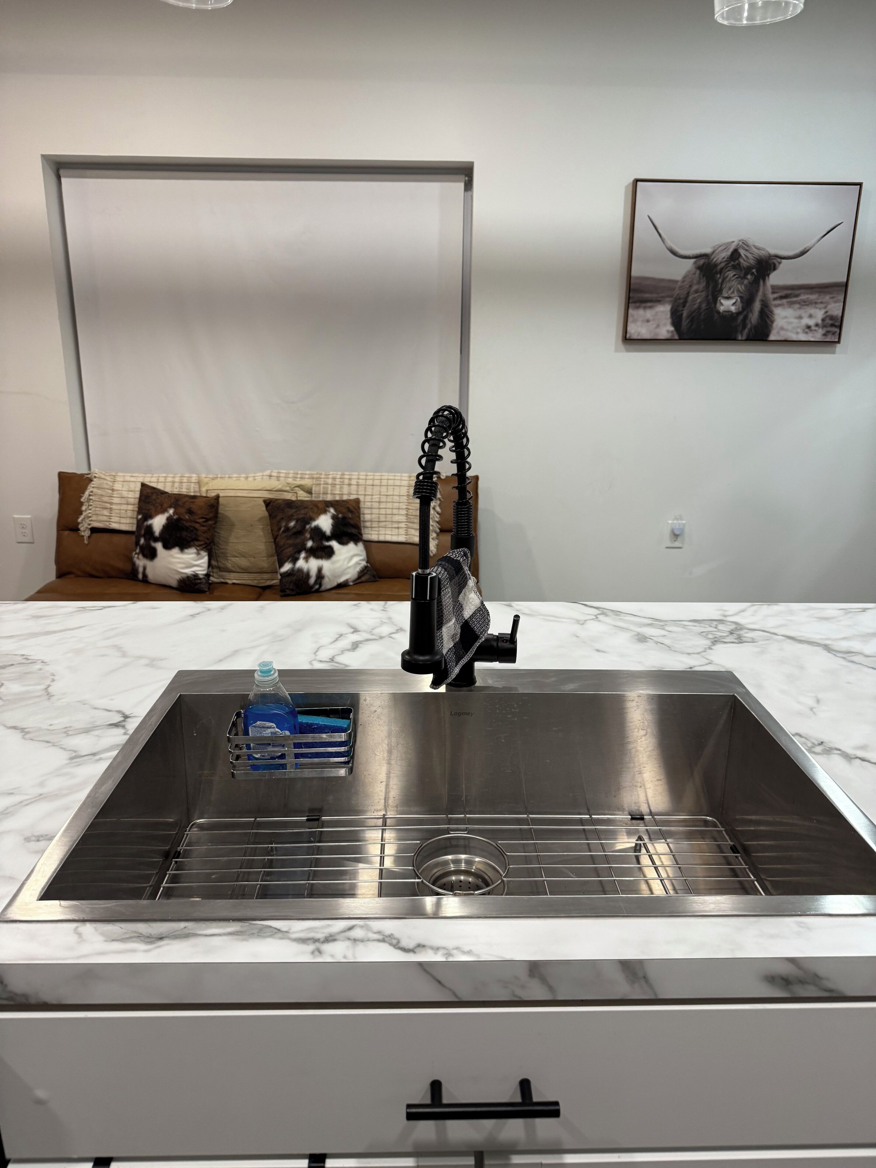 A modern kitchen with a stainless steel sink, a marble countertop, and a built-in oven.