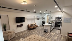 Una sala de estar moderna con una cama grande, un sofá, un televisor y una cocina equipada con microondas y horno.