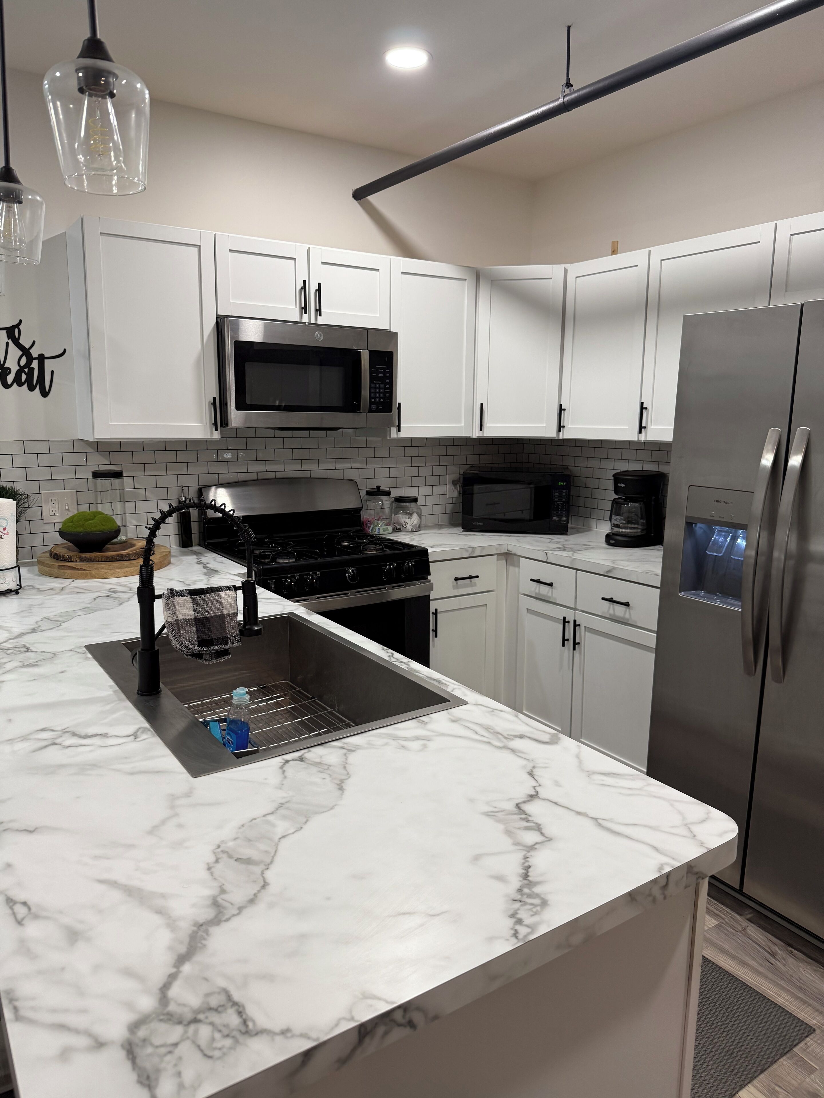 A modern kitchen with white cabinets, a stainless steel refrigerator, a microwave, and a gas stove.