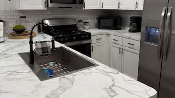 A modern kitchen with white cabinets, a stainless steel refrigerator, a microwave, and a gas stove.