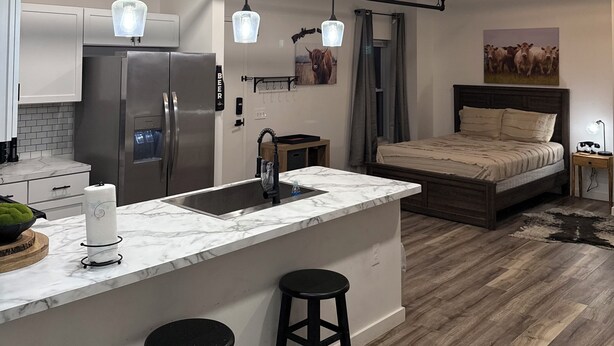 Una cocina moderna con una isla central, electrodomésticos de acero inoxidable, iluminación colgante y suelo de madera.
