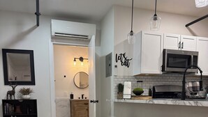Una cocina moderna con armarios blancos, encimera negra y microondas de acero inoxidable. Hay dos taburetes negros y un banco de madera.