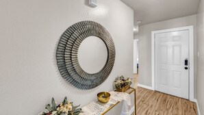 Un couloir orné d’une décoration murale circulaire, avec une porte blanche et une petite table sur laquelle se trouvent un bol et des fleurs.