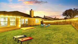 Un jardin avec une clôture en bois, une terrasse avec des chaises et une maison bien éclairée.