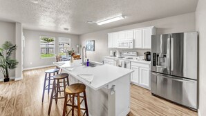 Une cuisine moderne avec des meubles blancs, un réfrigérateur en acier inoxydable et un îlot central doté de tabourets.