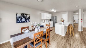 Une cuisine moderne avec des meubles blancs, un îlot central et un coin repas comprenant une table et des chaises en bois.