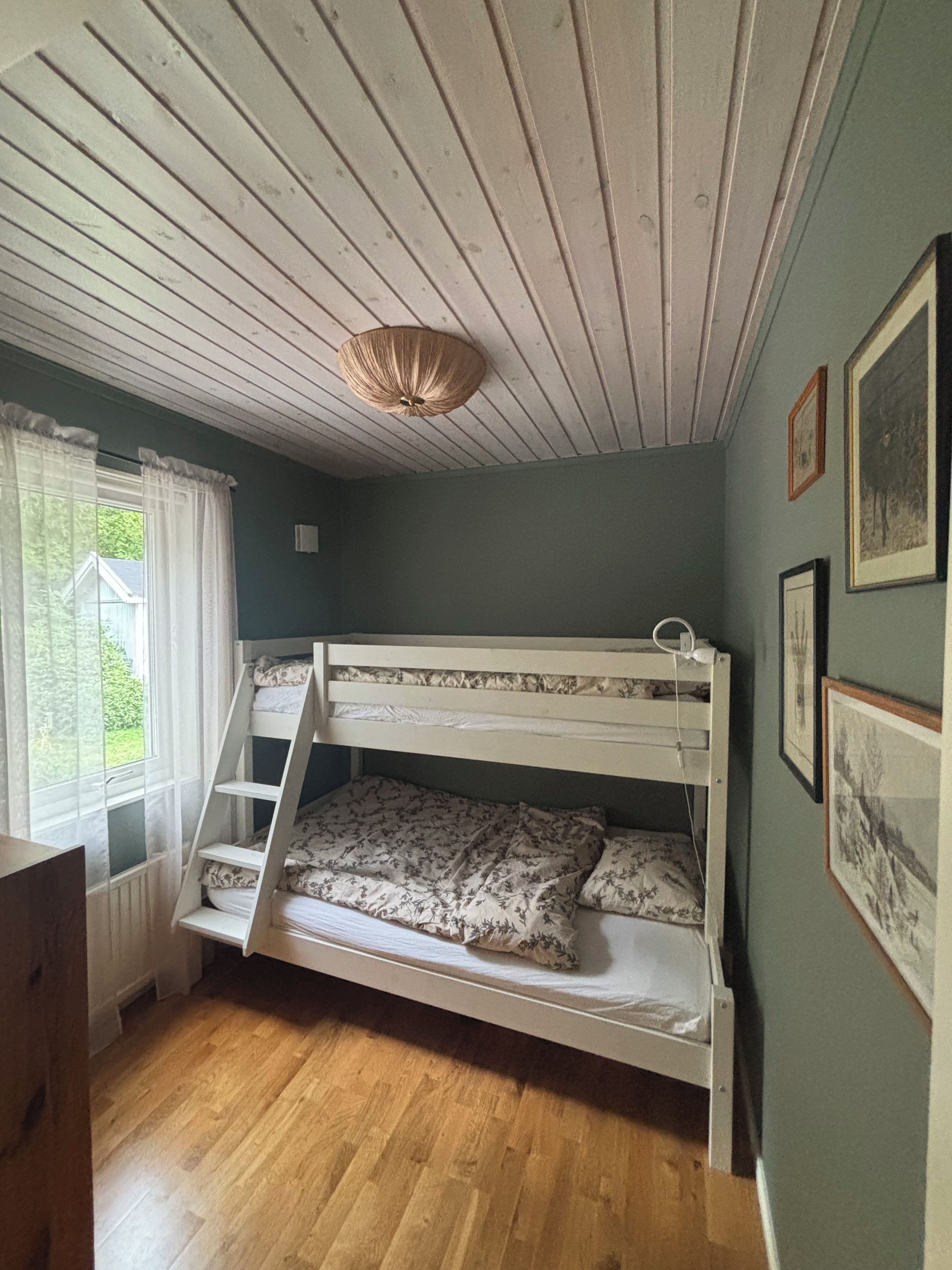 Een slaapkamer met een stapelbed, een houten trap, een raam met gordijnen en ingelijste foto's aan de muur.