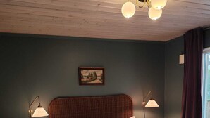 A bedroom with a wooden headboard, a white bedspread, two bedside lamps, a framed picture on the wall, and a window with curtains. - Stylish Lakehouse retreat with views over Djulö (Katrineholm)