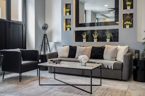 A modern living room with a grey sofa, black and white cushions, a coffee table with books and a vase, and a floor lamp.