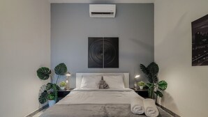 A modern hotel room with a large bed, a wall-mounted air conditioner, a cityscape artwork, and potted plants. - Designer Boutique 2-Bedroom Apartment in the Heart of Old San Juan (San Juan)
