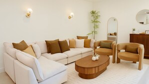 A modern living room with a sectional sofa, two armchairs, a wooden coffee table, and a large mirror. - The Ultimate OC Stay – NEW Stylish 6BR Home Perfect for Families & Groups! (Santa Ana)