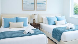 A hotel room with two beds, each with blue bedding and pillows, a nightstand with a lamp, and two framed pictures on the wall. - The Ultimate OC Stay – NEW Stylish 6BR Home Perfect for Families & Groups! (Santa Ana)