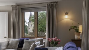 Una sala de estar con un sofá, una ventana con cortinas, una lámpara y un florero con flores.