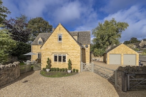 A stone house with a gravel driveway, a wooden gate, and a small garden with potted plants.