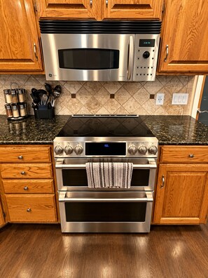 A kitchen with a stainless steel microwave, oven, and stovetop. There are wooden cabinets and a tiled backsplash.