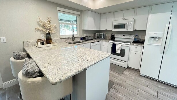 Una cocina moderna con armarios blancos, encimera de granito, horno empotrado, microondas y refrigerador.
