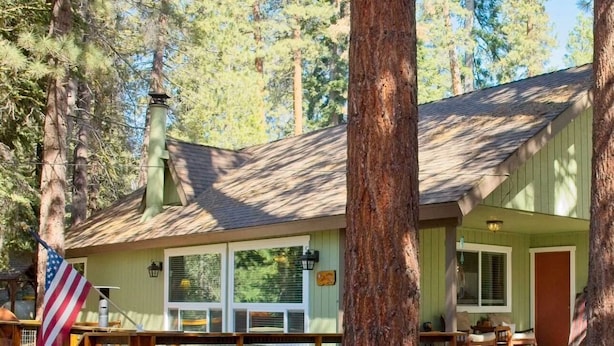 A cabin with a deck, a covered porch, and a flag. - One acre with a fire pit, kids play area, treehouse, zipline, pets welcome (Springville)
