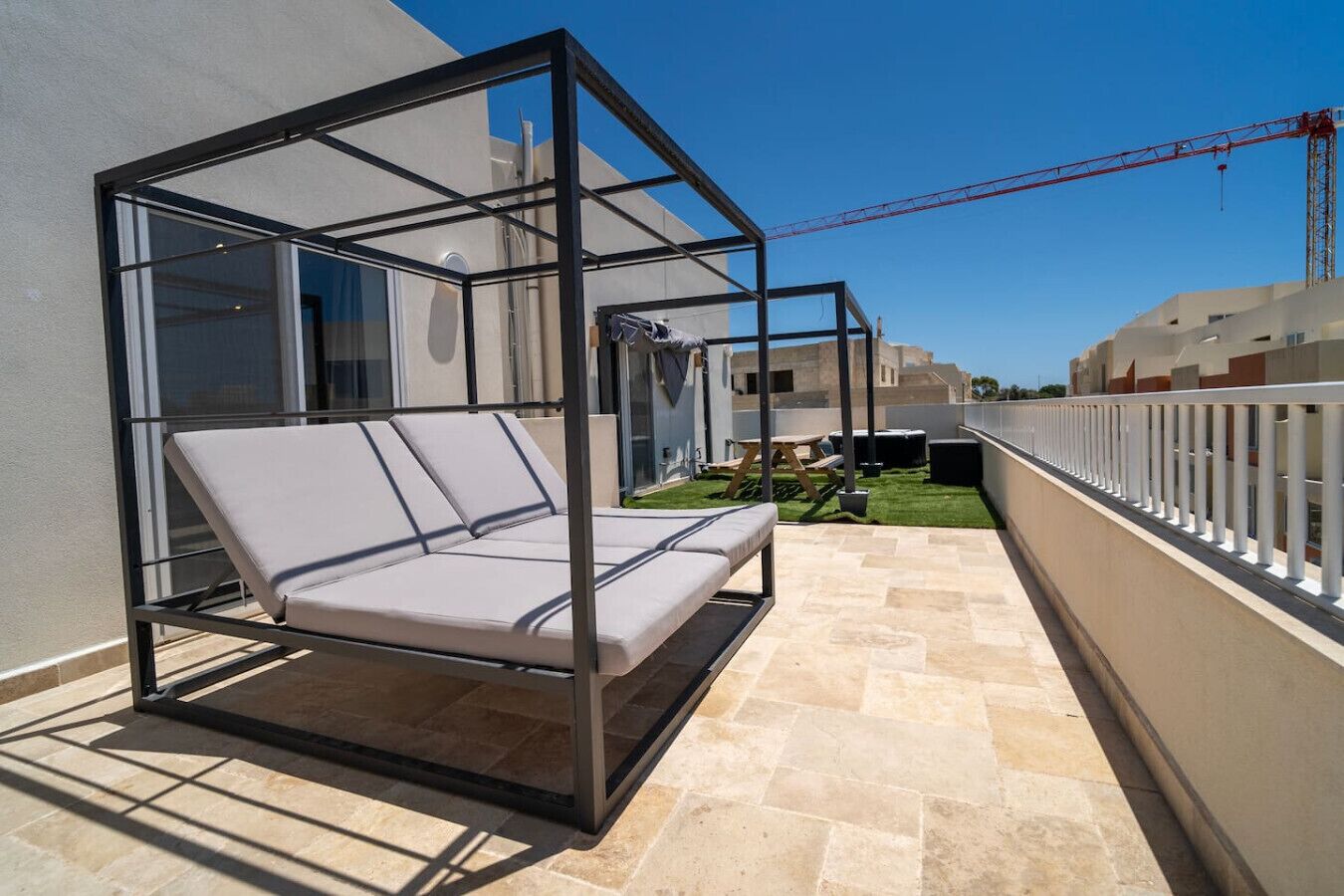 Ein Balkon mit Glasveranda, einer gepolsterten Sitzecke und Blick auf eine Baustelle im Hintergrund.