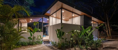 Una casa moderna con un porche cubierto, rodeada de plantas tropicales.