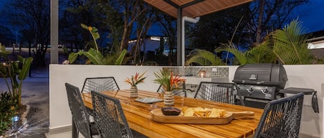 Une terrasse extérieure avec une table en bois, des chaises en osier noir, un barbecue et des plantes en pot.