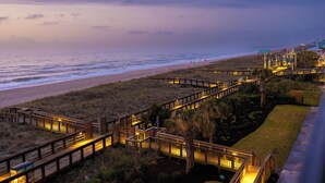 A coastal hotel with a wooden boardwalk leading to beach access, a well-maintained lawn, and a view of the ocean. - Beachfront Luxe • Sleeps 6 • Best Location in CB! (Carolina beach)