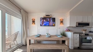 A modern kitchen with a wooden table, built-in appliances, and a TV mounted above the counter. - Beachfront Luxe • Sleeps 6 • Best Location in CB! (Carolina beach)