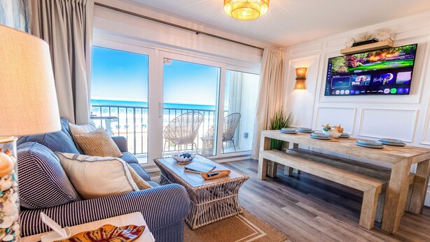A modern living room with a sofa, a coffee table, a TV, and a balcony with a view. - Beachfront Luxe • Sleeps 6 • Best Location in CB! (Carolina beach)