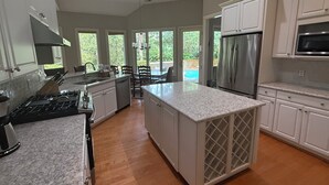 A spacious kitchen with granite countertops, stainless steel appliances, and large windows offering views of a backyard. - WALK TO BEACH! Pool/spa fenced yard. (Hilton Head Island)