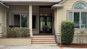 A house with a front porch, a set of steps leading to the entrance, and a small garden area with bushes. - WALK TO BEACH! Pool/spa fenced yard. (Hilton Head Island)