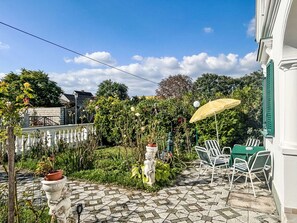 A courtyard with a stone-tiled patio, white chairs, a table, and a yellow umbrella. - Großmutters Ferienhaus by Interhome (Mörbisch am See)