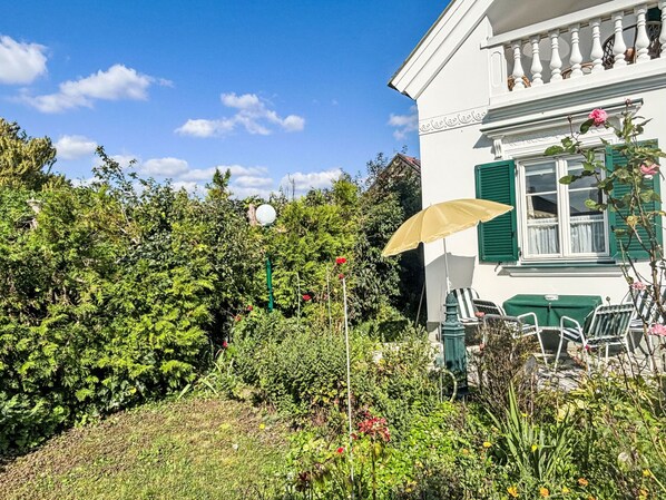 A white building with green shutters, a garden with various plants and flowers, and outdoor furniture. - Großmutters Ferienhaus by Interhome (Mörbisch am See)