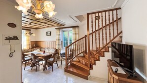 Ein geräumiger Essbereich mit einem Holztisch und Stühlen, einer Chandelüster und einer Treppe mit Holzläufer, die zu einer Zwischenebene führt.
