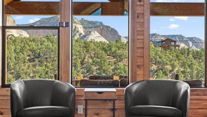 A cabin with two leather chairs facing a large window overlooking a mountainous landscape. - The Vue: Perfect Base for Zion & Bryce Adventures (Orderville)