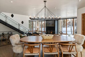 Une salle à manger spacieuse, dotée d’une grande table ronde et de chaises en bois, d’un lustre et d’un escalier menant à un niveau supérieur.