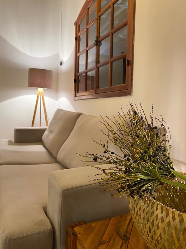 Uma sala de estar com sofá, luminária e uma planta decorativa em cesta de palha.