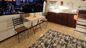 Un salon moderne doté d’un grand téléviseur diffusant une vue sur la ville, d’une table à manger en bois avec des chaises, d’un coin salon confortable avec un canapé et d’un tapis à motifs.