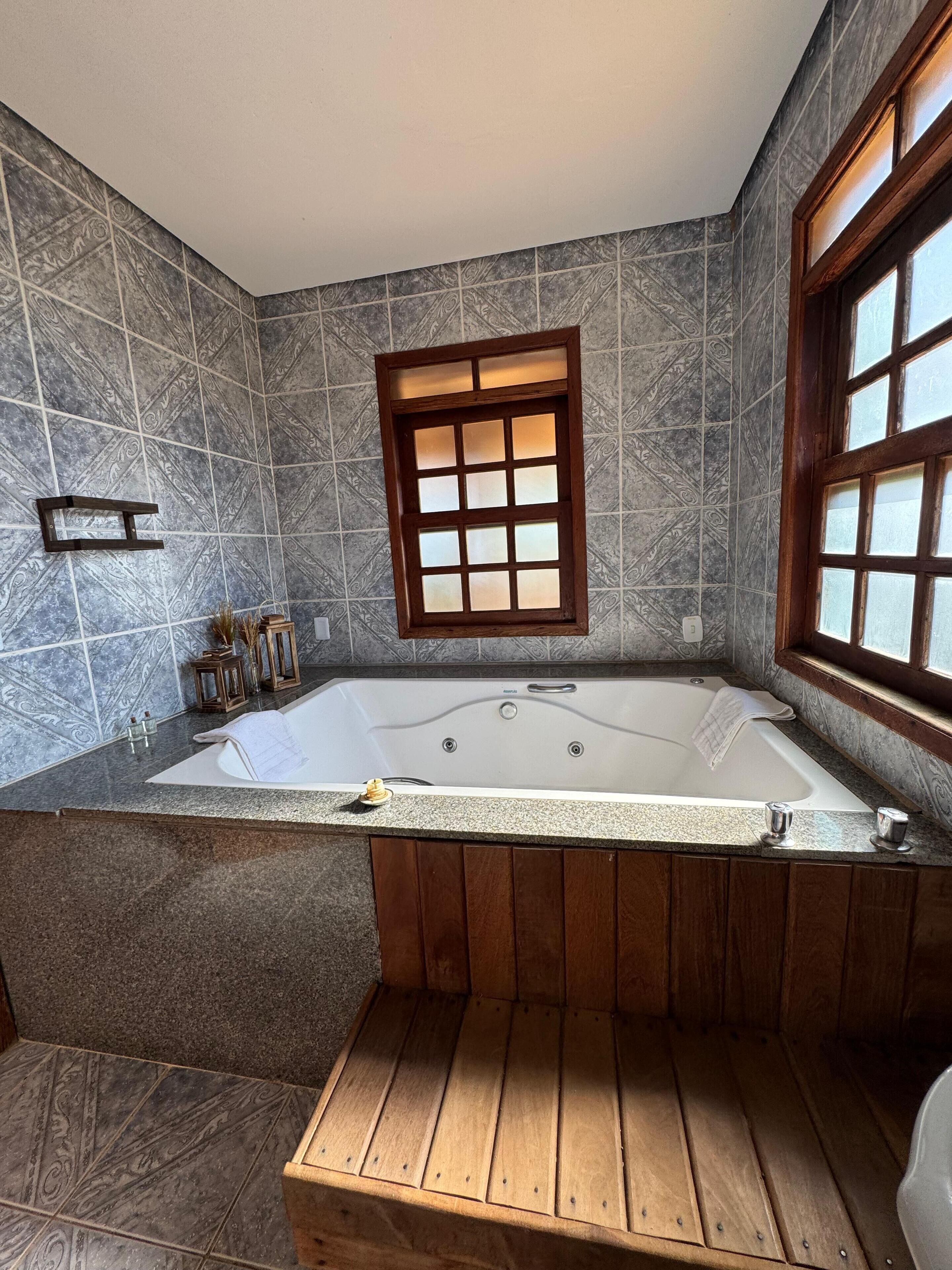 Um banheiro com uma banheira de pedestal, uma janela com moldura de madeira e parede revestida de azulejos.