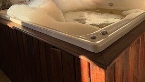 Un bain à remous avec vue sur les montagnes, des murs de style cabane en bois et une fenêtre avec des rideaux.