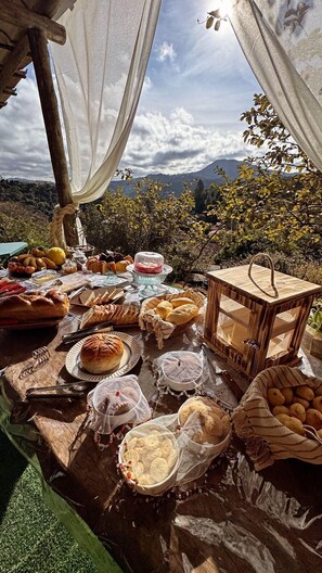 Ein Essbereich im Freien mit verschiedenen Brotsorten und Gebäcken auf einem Holztisch, vor einer malerischen Berglandschaft.