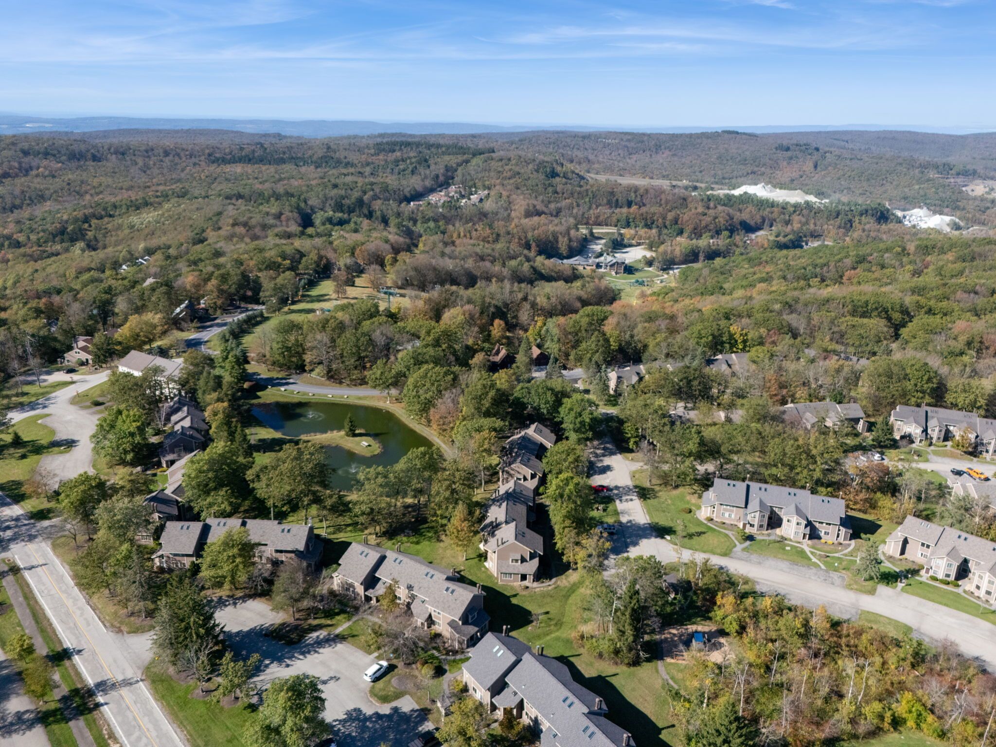 An aerial view of a residential area with houses, roads, and a pond.