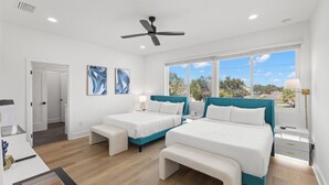 A modern bedroom with two beds, a ceiling fan, and large windows offering a view of the outdoors.
