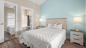 Camera da letto con un letto grande, una testata in legno, due comodini con lampade, uno specchio e una porta che dà su un'altra stanza.