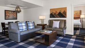 Un salón moderno con un sofá gris, un sillón de cuero marrón y una mesita de centro. Hay dos lámparas de pared y un cuadro sobre el sillón.
