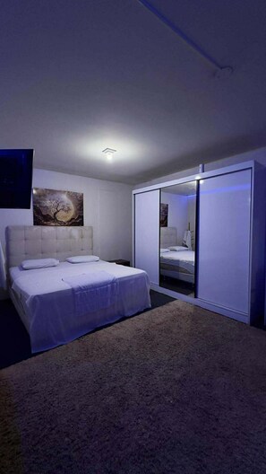 A bedroom with a bed, a nightstand, a painting on the wall, and a sliding closet door. - Londrina Hostel (Londrina)