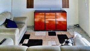 A living room with a flat-screen TV mounted on the wall, a red cabinet below, and a beige sofa with a remote control on it.