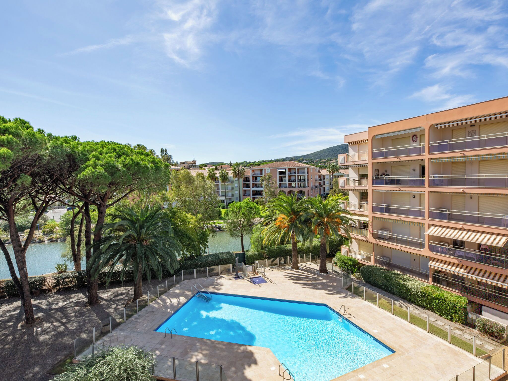 A swimming pool surrounded by trees and a multi-story building with balconies.