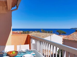 A balcony with a table set for dining, overlooking a coastal view with buildings and the sea.