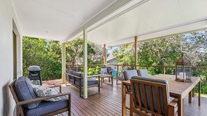 A covered outdoor deck with wooden furniture, a table, and a lantern. - Moonee Stayz - Bungalow 5 (Moonee Beach)
