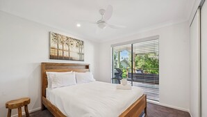 A bedroom with a wooden bed, a ceiling fan, a window with blinds, and a small wooden stool. - Moonee Stayz - Bungalow 5 (Moonee Beach)